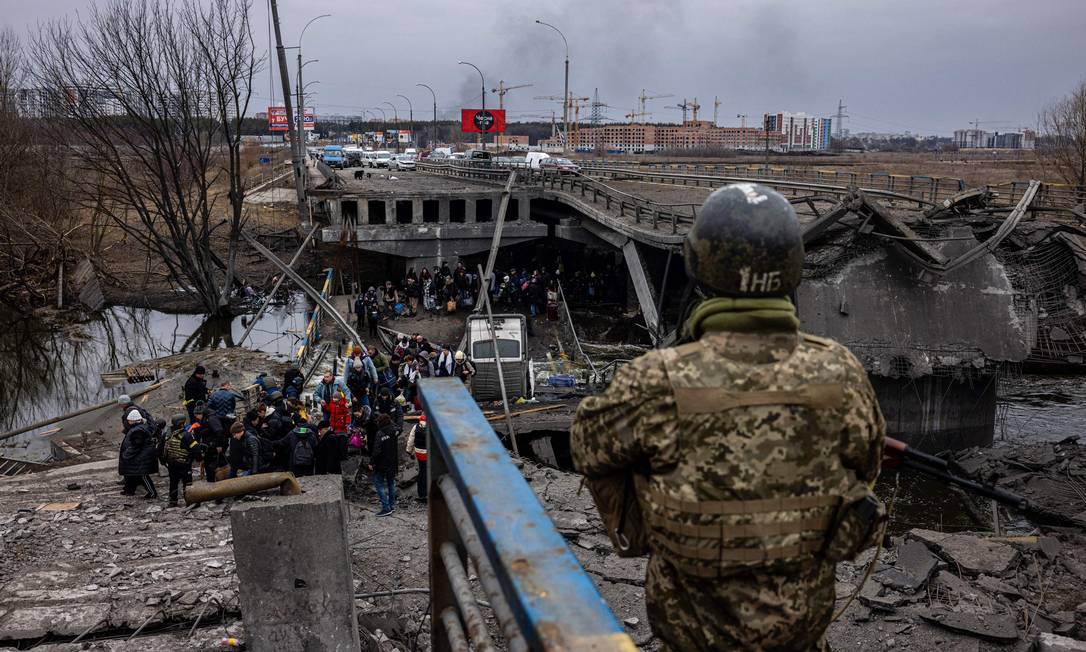 Um militar ucraniano observa os evacuados atravessarem uma ponte destruída enquanto fogem da cidade de Irpin Foto: DIMITAR DILKOFF / AFP