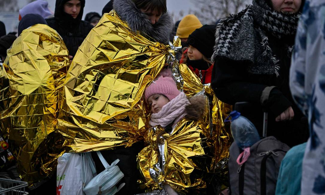 Famílias tentam se aquecer com manta térmica em estação de trem da Ucrânia, na fronteira com a Polônia Foto: LOUISA GOULIAMAKI / AFP