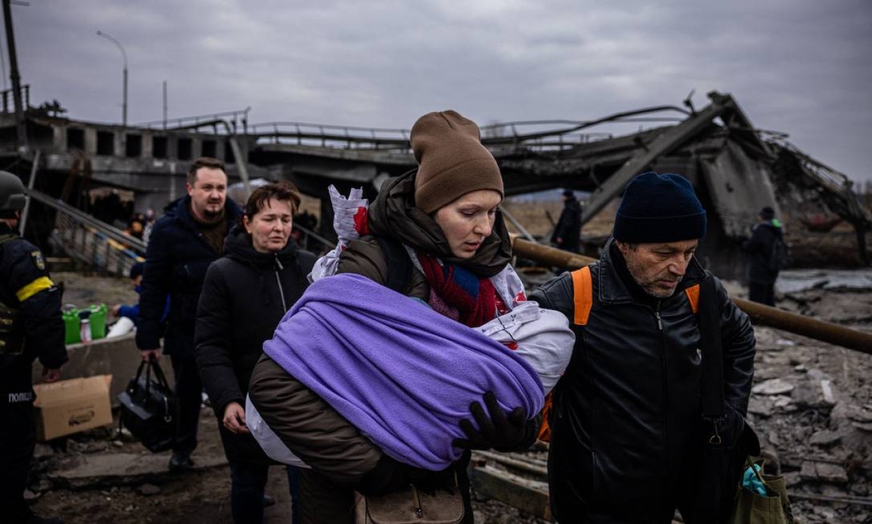 Mulher atravessa ponte destruída ao fugir da cidade de Irpin, a noroeste de Kiev, com bebê no colo Foto: DIMITAR DILKOFF / AFP