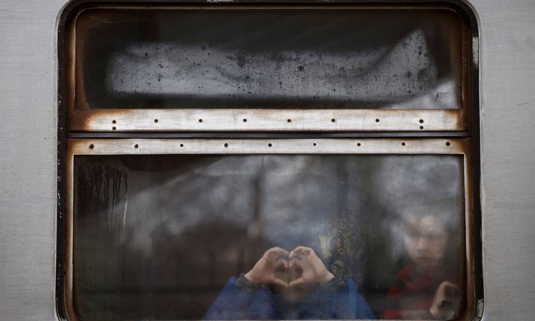 Criança faz sinal de coração com as mãos na janela de trem que parte de Lviv, na Ucrânia, em busca de refúgio Foto: YARA NARDI / REUTERS