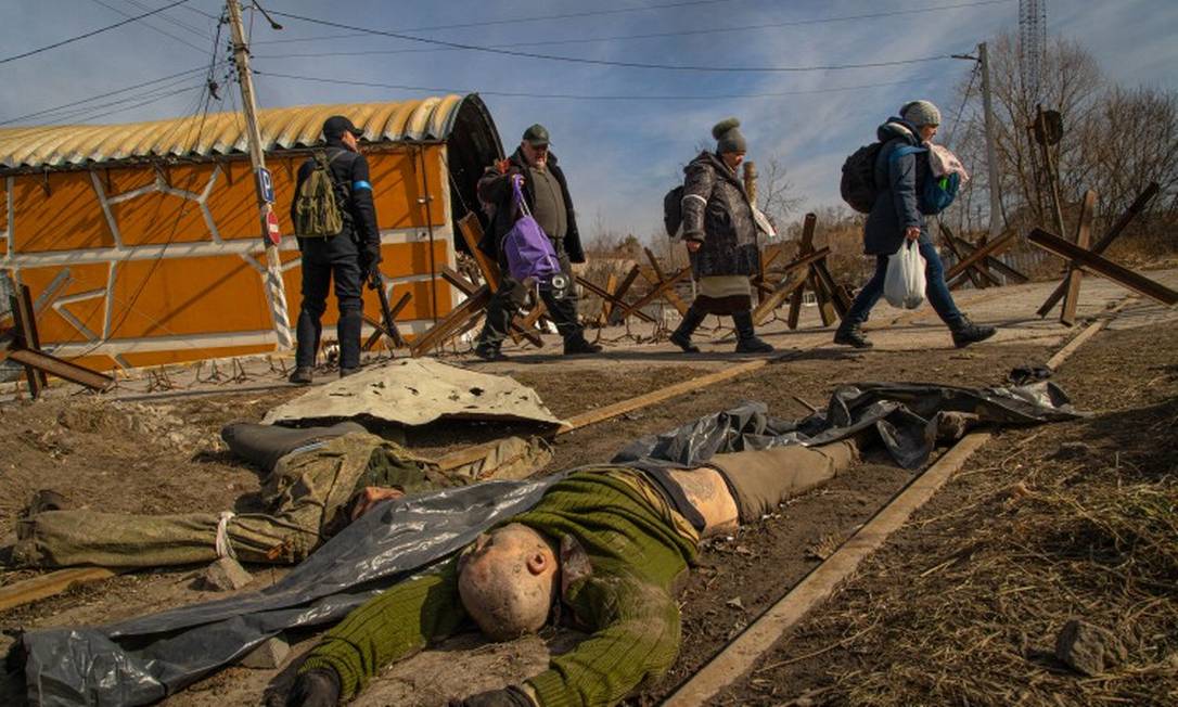 Civis ucranianos passam pelos corpos de dois soldados russos entre as cidades de Irpin e Bucha, perto de Kiev, onde as forças de Ucrânia e Rússia se enfrentam há mais de uma semana Foto: YAN BOECHAT / .
