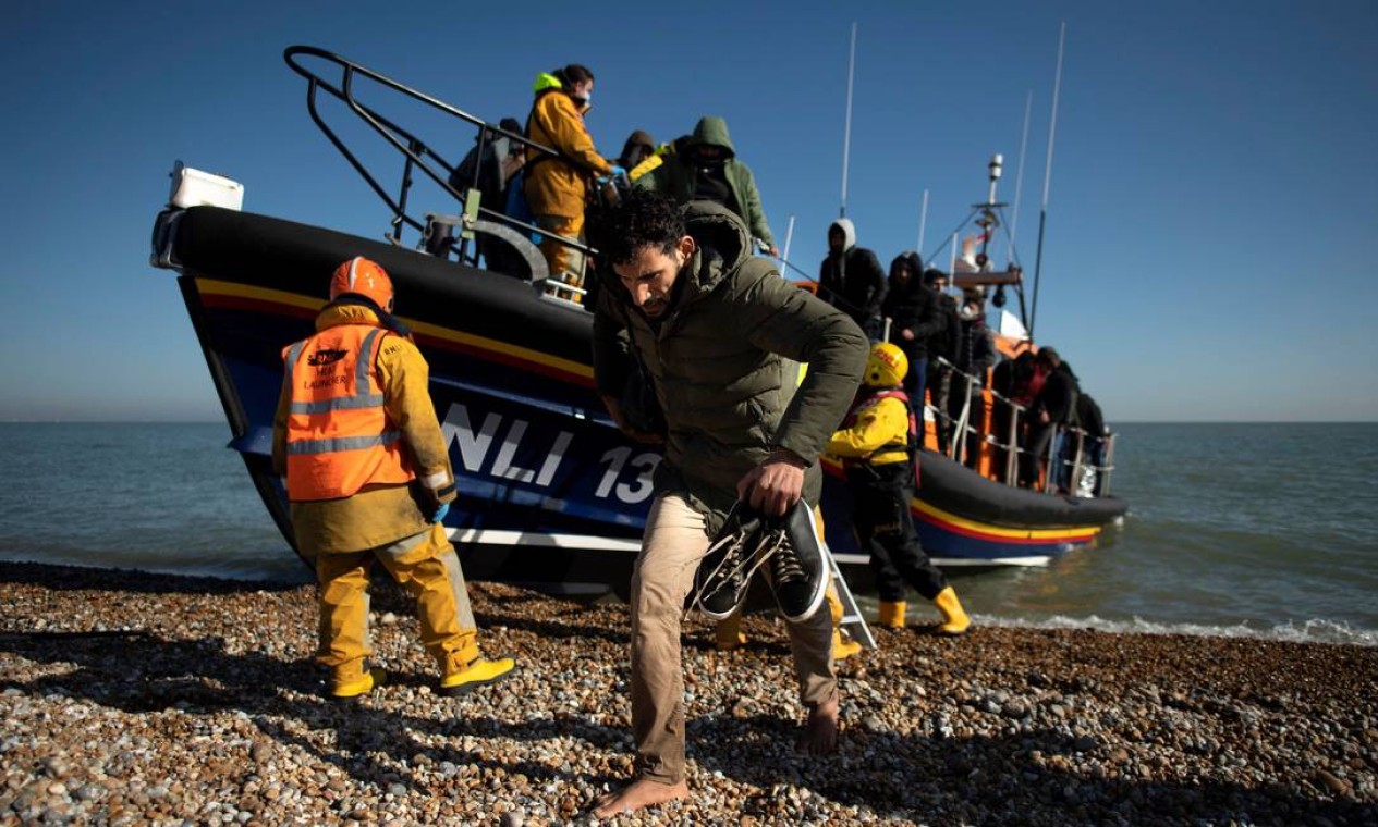 Migrantes, apanhados no mar tentando cruzar o Canal da Mancha, são ajudados por um bote salva-vidas da RNLI (Royal National Lifeboat Institution) depois de serem trazidos para terra em Dungeness, na costa sudeste da Inglaterra Foto: BEN STANSALL / AFP