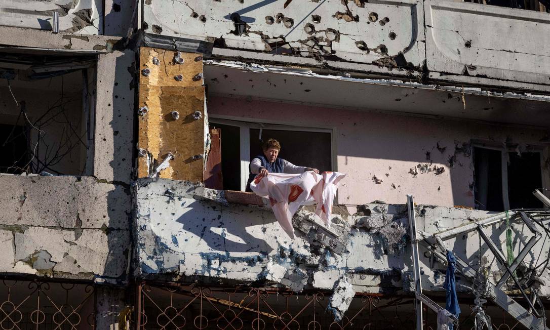 Moradora limpa varanda em prédio residencial danificados por bombardeio em Kiev, onde explosões poderosas abalaram bairros residenciais na madrugada Foto: FADEL SENNA / AFP