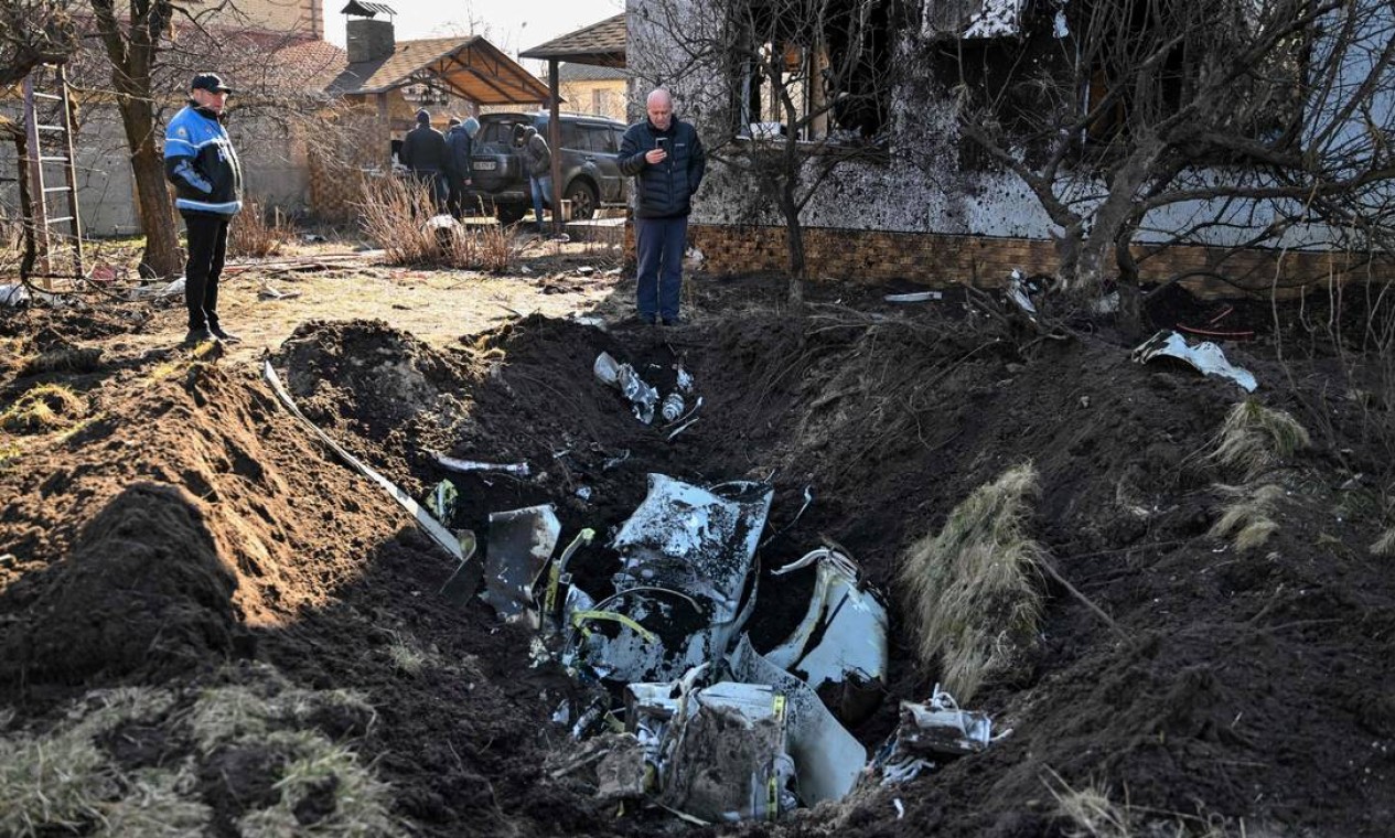Homem tira fotos dos restos de um míssil no quintal de uma casa atingida por um bombardeio no distrito de Osokorky, no sudeste de Kiev Foto: GENYA SAVILOV / AFP