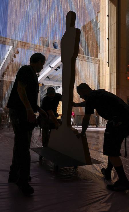Trabalhadores movem estátuas do Oscar pelo tapete vermelho enquanto os preparativos para o Oscar continuam em Los Angeles Foto: MIKE BLAKE / REUTERS