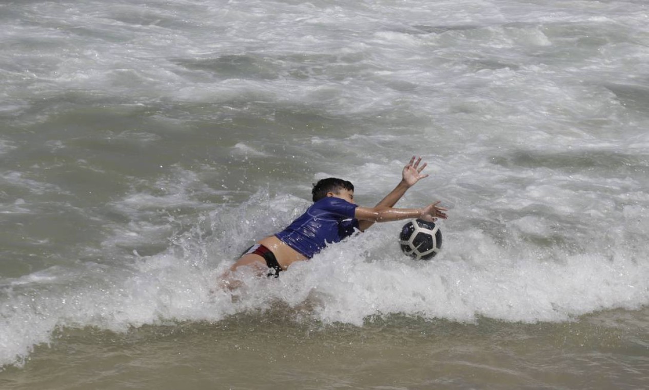 Criança brinca de futebol à beira-mar Foto: Domingos Peixoto / Agência O Globo
