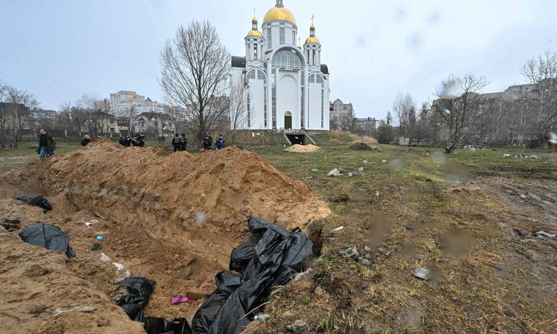 Uma vala comum de corpos está loalizada atrás de uma igreja, em Bucha Foto: SERGEI SUPINSKY / AFP