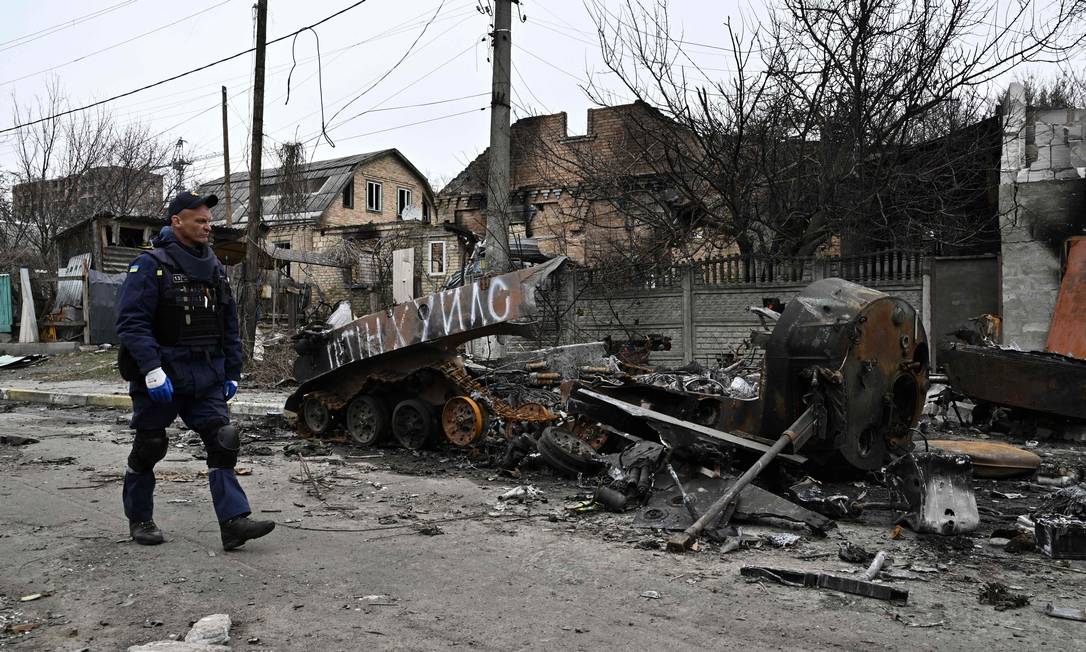 Engenheiro do Serviço de Emergências da Ucrânia caminha ao lado de destroços de veículos blindados nas ruas de Bucha Foto: GENYA SAVILOV / AFP
