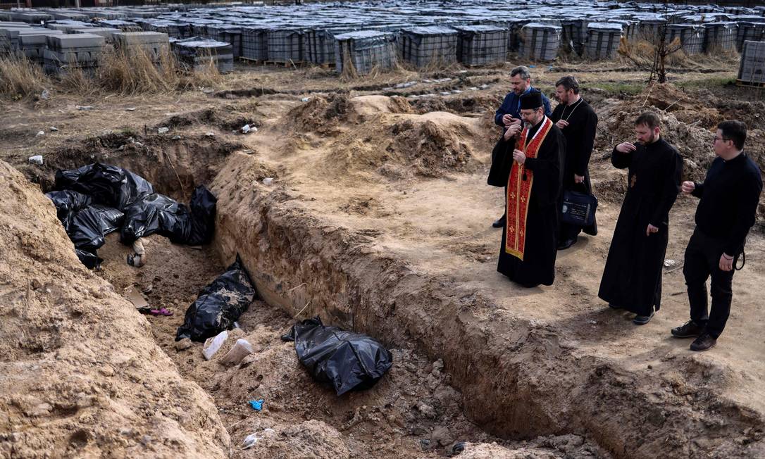 Religiosos oram em frente a uma vala comum em Bucha, cidade onde centenas de corpos foram encontrados com sinais de execução após a saída dos soldados russos
Foto: Ronaldo Schemidt / AFP