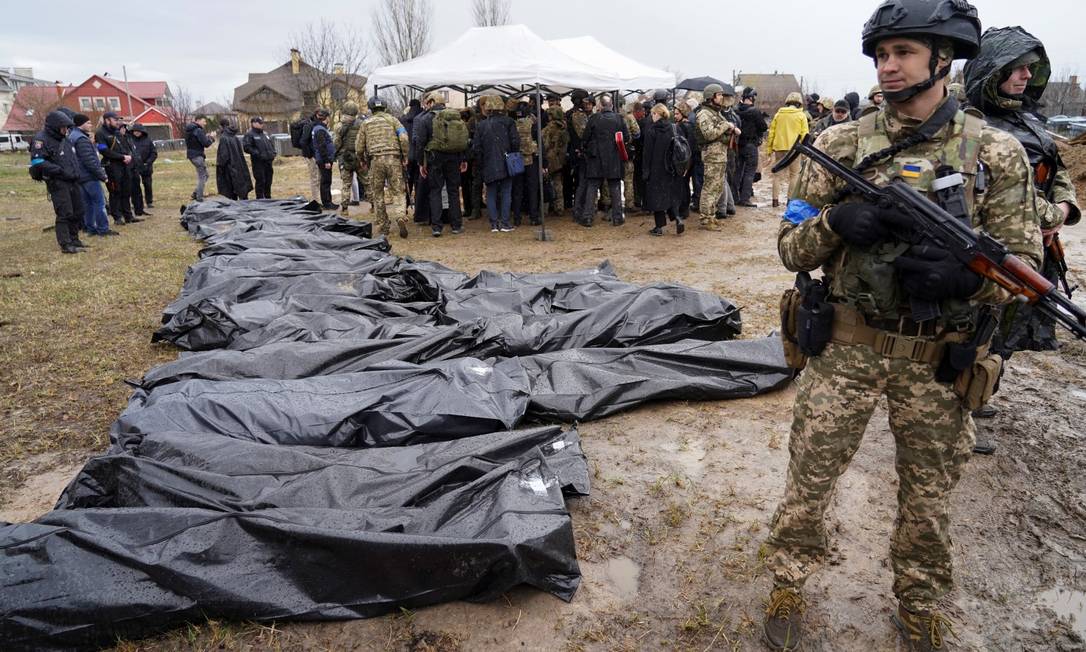 Militares ucranianos montam guarda ao lado de corpos que foram exumados de uma vala comum na cidade de Bucha, enquanto o ataque da Rússia à Ucrânia continua Foto: JANIS LAIZANS / REUTERS