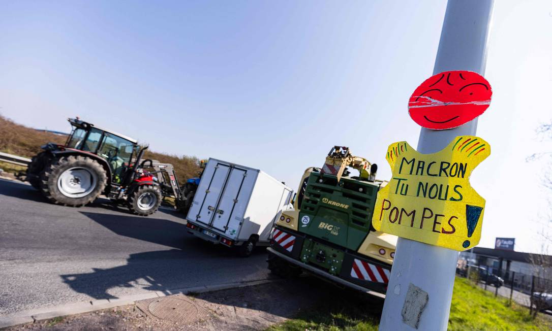 “Macron, você nos enche”, diz trocadilho com verbo usado para “encher o tanque” em cartaz de protesto de agricultores que pedem congelamento dos preços do diesel usado em tratores em Caen Foto: SAMEER AL-DOUMY / AFP