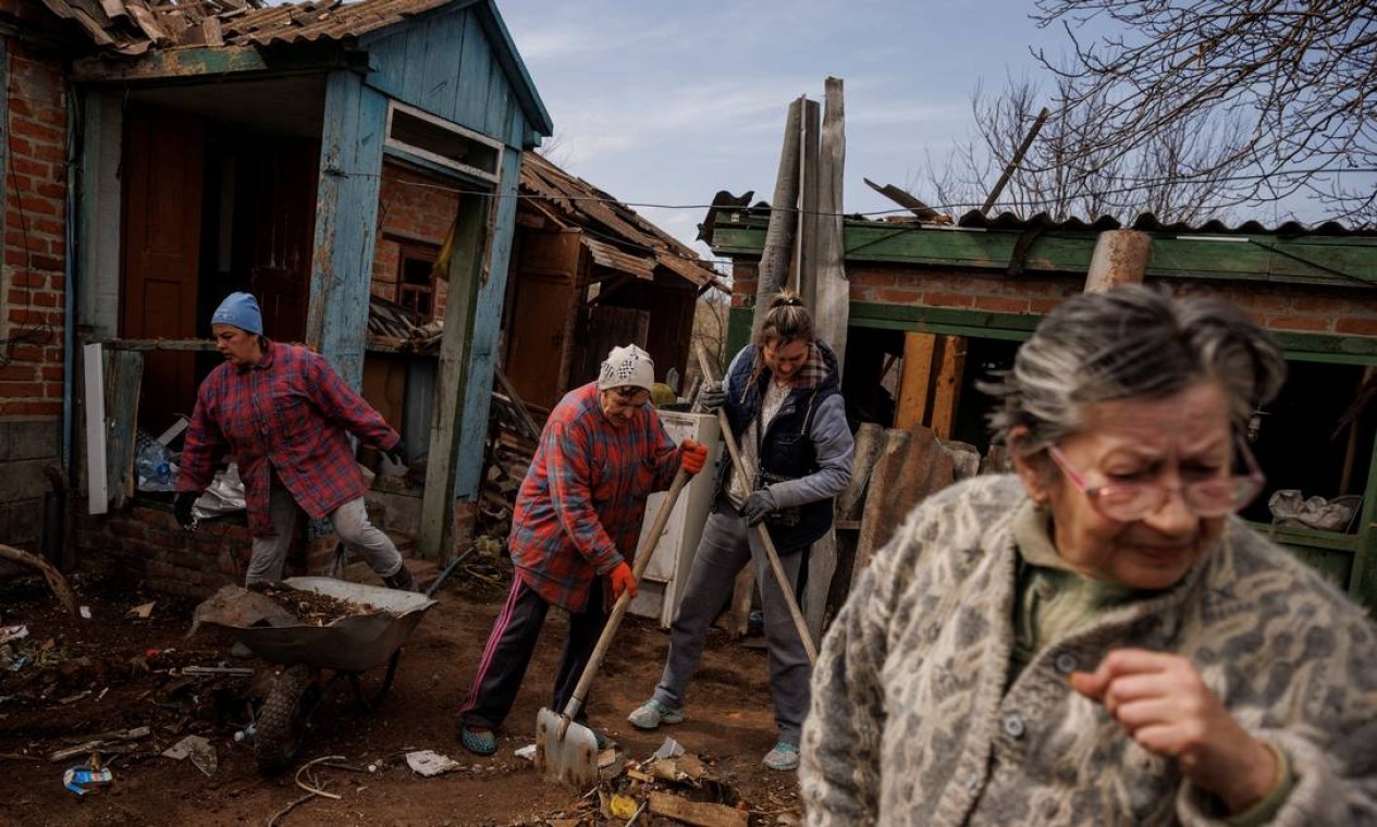 Moradores ajudam vizinha a limpar seu quintal depois que sua casa foi danificada por um bombardeio das tropas russas na vila de Yakovlivka, nos arredores de Kharkiv Foto: THOMAS PETER / REUTERS