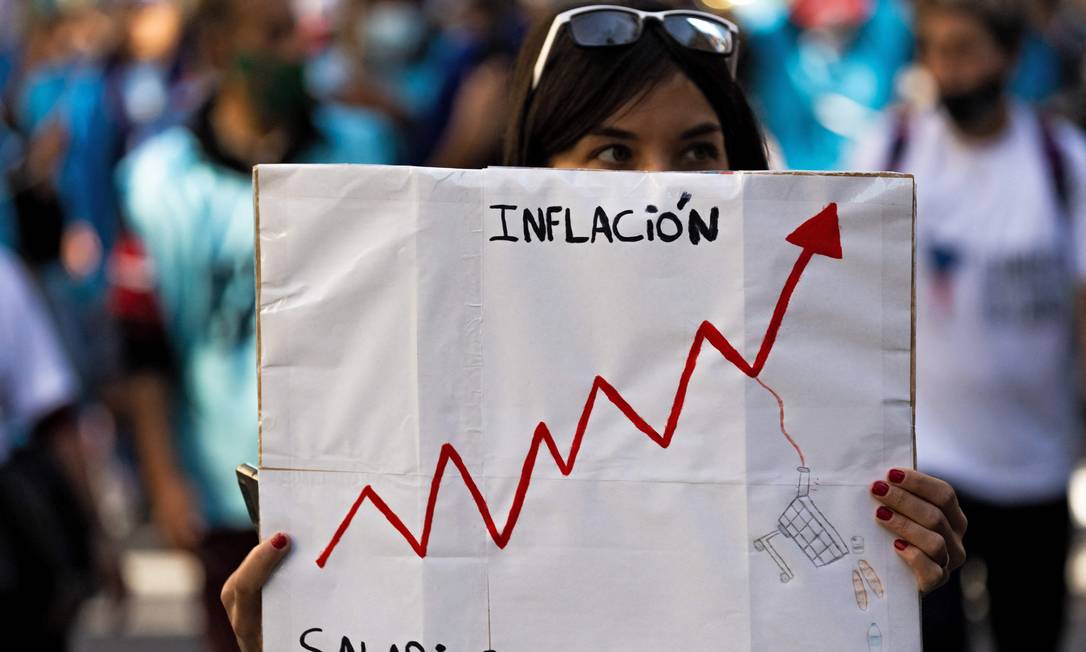 Mulher segura cartaz com gráfico em que inflação aparece subindo e salários continuam estagnados Foto: TOMAS CUESTA / AFP