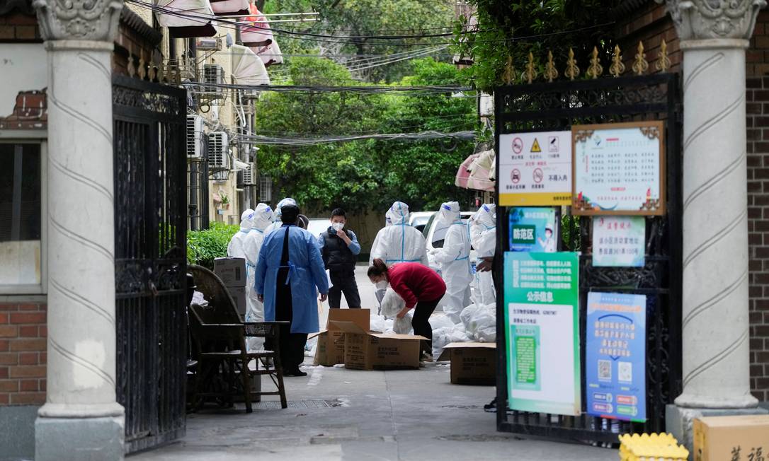 Usando trajes de proteção, trabalhadores caminham por área residencial em meio à pandemia de coronavírus, em Xangai Foto: ALY SONG / REUTERS