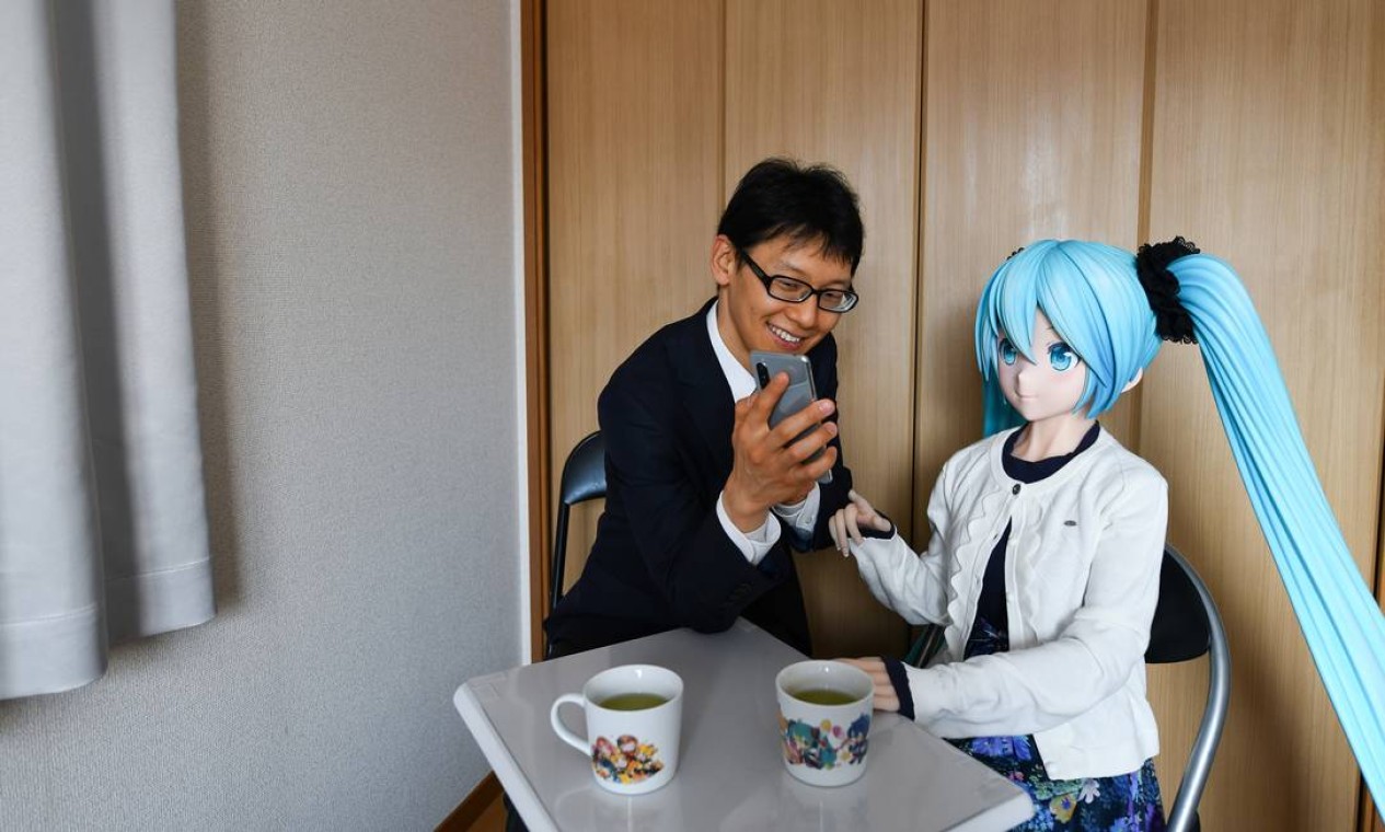 Akihiko Kondo mostra seu telefone para a boneca em tamanho real de Hatsune Miku, a estrela pop virtual, com quem se casou em 2018. Além de Kondo, milhares de outros estão tendo relacionamentos fictícios Foto: NORIKO HAYASHI / NYT