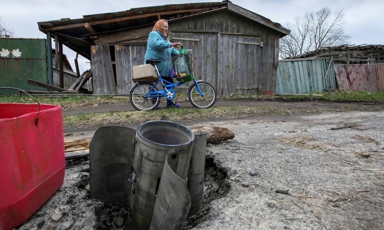 Mulher passa por um projétil de lançamento de vários mísseis na vila de Kukhari, região de Kiev Foto: STRINGER / REUTERS