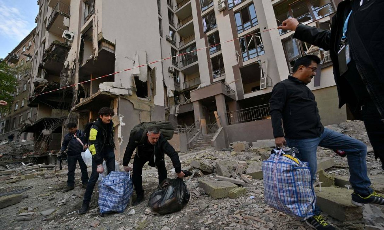 Moradores carregam seus pertences ao deixarem prédio danificado por ataques russos, em Kiev Foto: SERGEI SUPINSKY / AFP