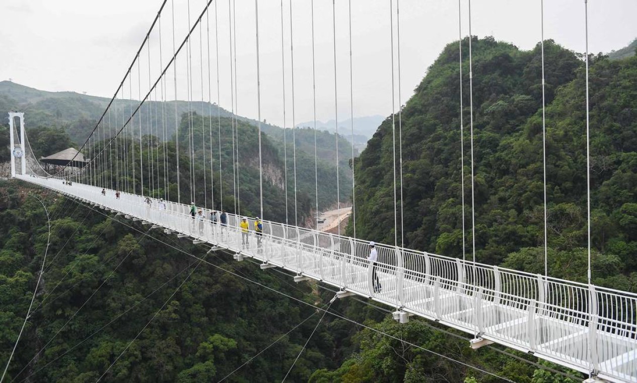 Visitantes caminham sobre ponte de vidro Bach Long, no Vietnã. Atração, lançada para turistas, tem cerca de 150 metros acima de um exuberante desfiladeiro coberto de selva Foto: NHAC NGUYEN / AFP