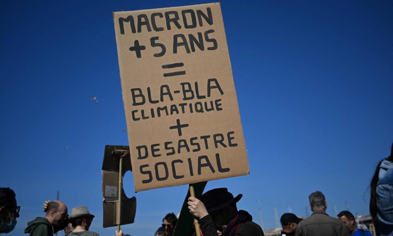Manifestante exibe um cartaz com com a frase "Macron + 5 anos = clima blá blá + desastre social" durante o Dia do Trabalho em Marselha, sul da França Foto: CHRISTOPHE SIMON / AFP