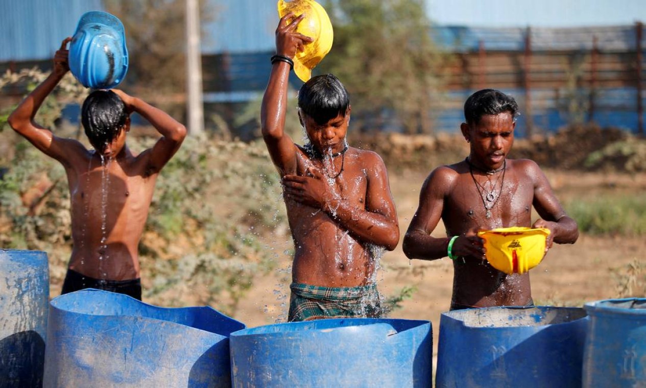 Trabalhadores usam seus capacetes para despejar água para se refrescar perto de um canteiro de obras nos arredores de Ahmedabad Foto: AMIT DAVE / REUTERS