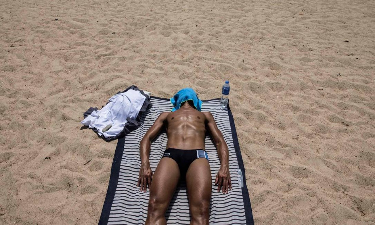 Homem toma banho de sol em uma praia em Hong Kong depois que o governo afrouxou as medidas de restrições da Covid-19 Foto: ISAAC LAWRENCE / AFP