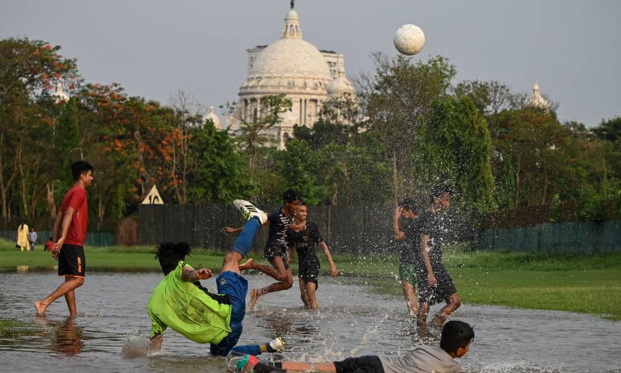 Jovens brincam em uma área alagada em um parque público chamado Maidan, em frente ao monumento Victoria Memorial, após uma breve chuva, em Calcutá, Índia Foto: DIBYANGSHU SARKAR / AFP