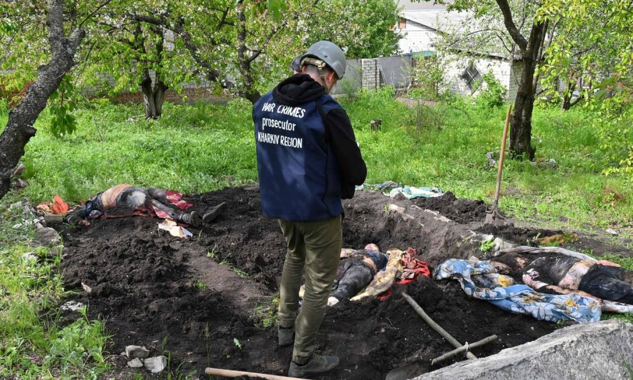 Investigador fica ao lado de corpos exumados de uma cova rasa, no quintal de uma casa na vila de Stepanky, perto de Kharkiv, Ucrânia Foto: SERGEY BOBOK / AFP