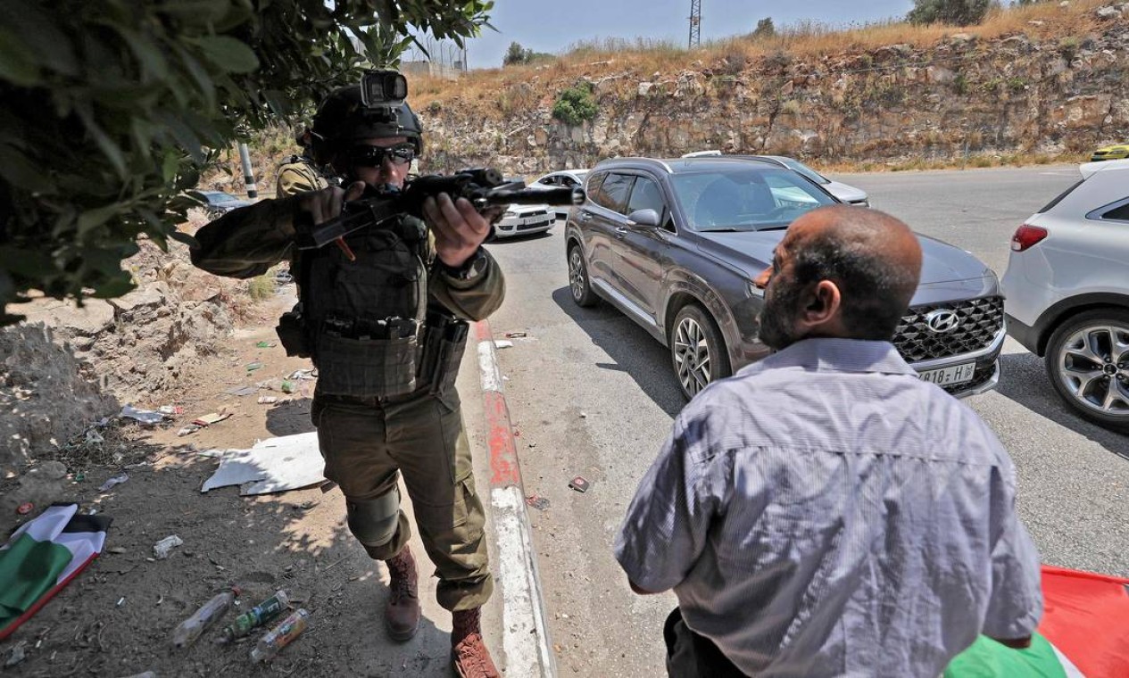 Soldado israelense interrompe o avanço de uma procissão fúnebre, de um homem palestino morto durante confrontos com as forças israelenses, em um posto de controle que sai da aldeia palestina de Nilin, a oeste de Ramallah, na Cisjordânia ocupada Foto: ABBAS MOMANI / AFP
