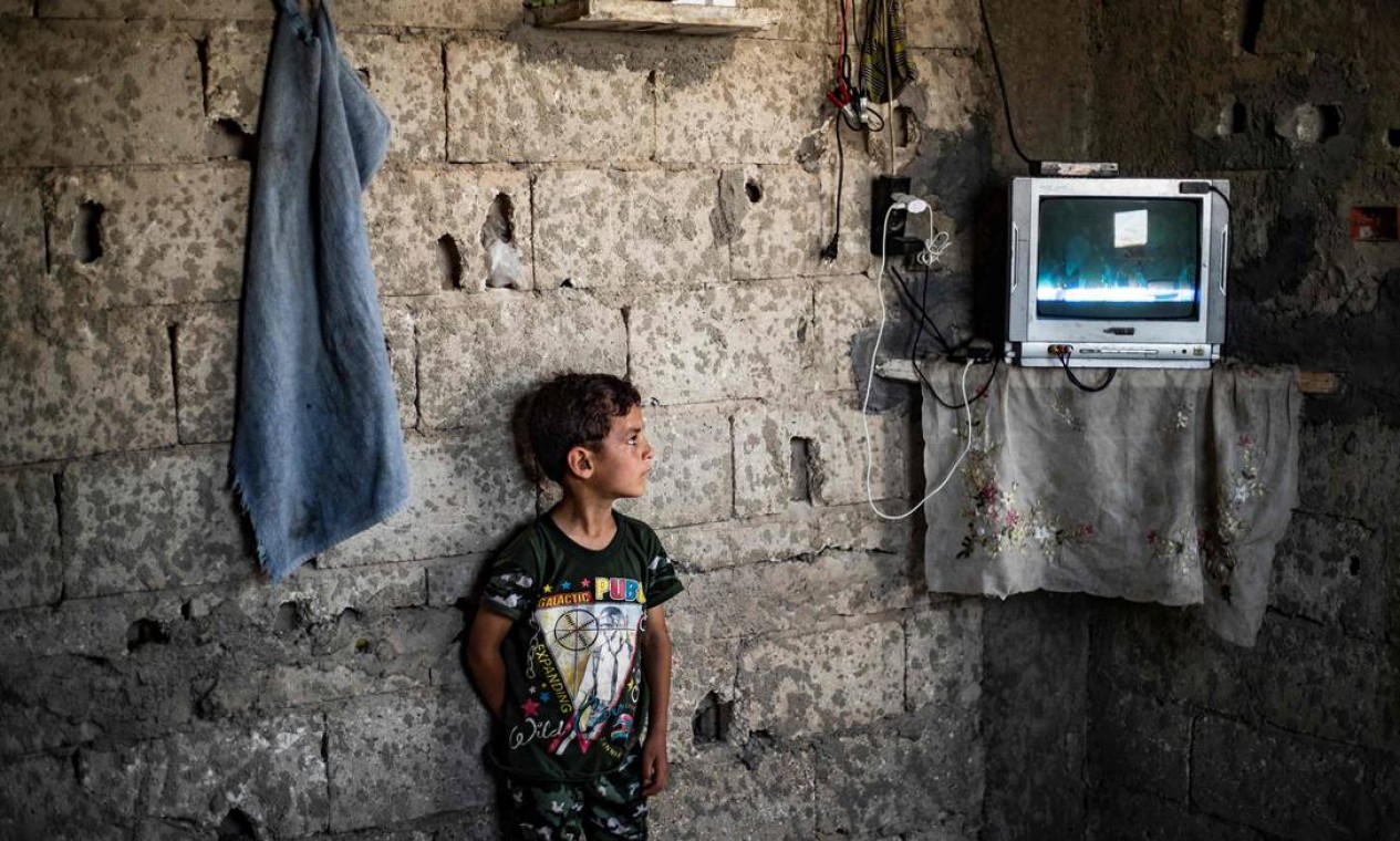 Menino sírio observa dentro do prédio danificado onde mora na cidade de Raqa, no norte do país. Ele foi deslocado pela guerra civil sua família de Deir Ez-Zor Foto: DELIL SOULEIMAN / AFP