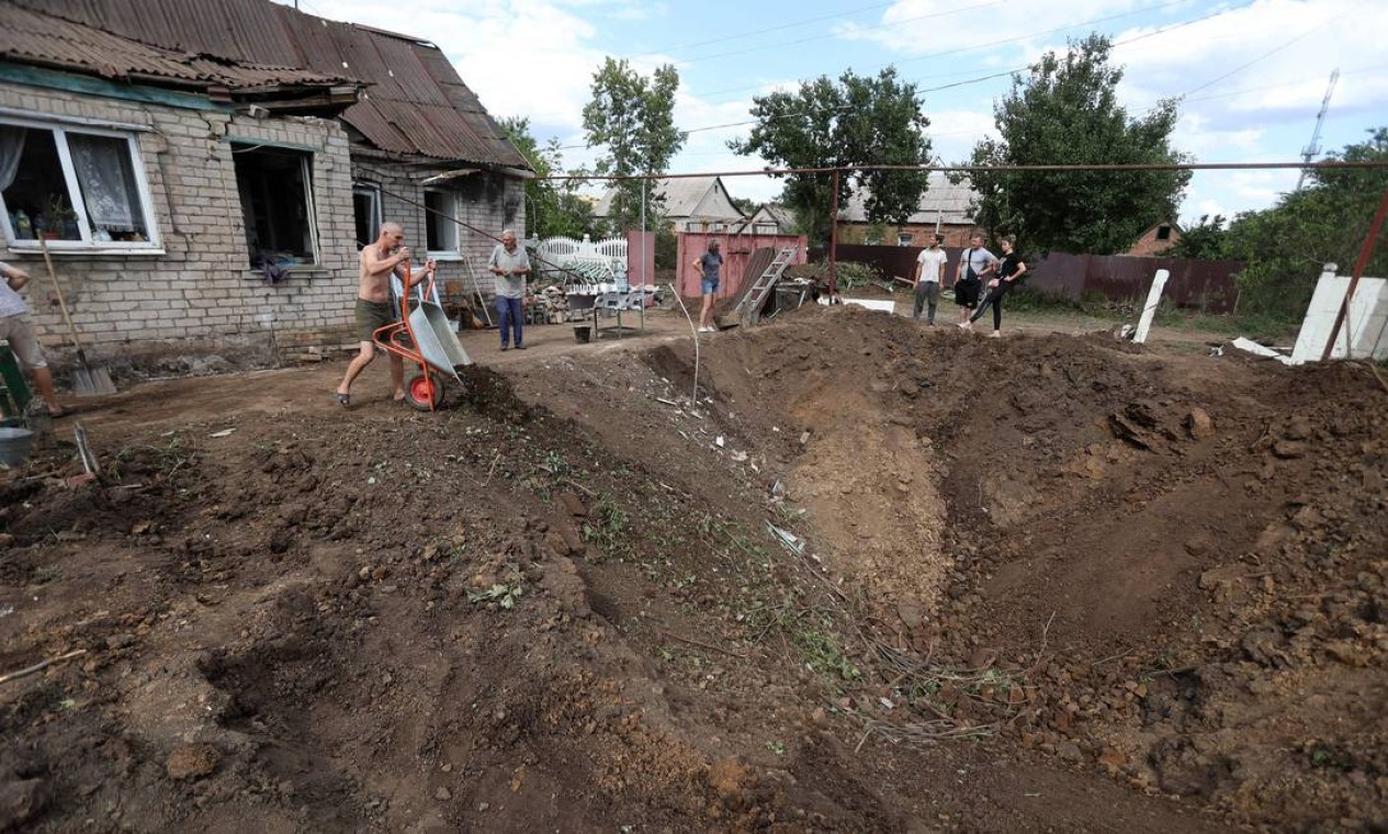 Moradores locais jogam destroços em uma cratera após um ataque russo em Kostyantynivka, região de Donetsk, Ucrânia Foto: ANATOLII STEPANOV / AFP