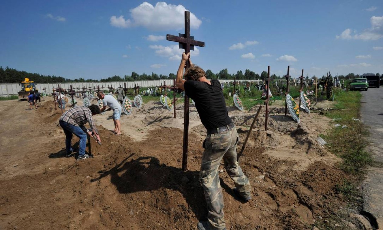 Trabalhadores comunitários enterram caixões durante funeral coletivo de pessoas não identificadas mortas no bimestre fevereiro-março de 2022 no cemitério de Bucha, Ucrânia Foto: SERGEI CHUZAVKOV / AFP