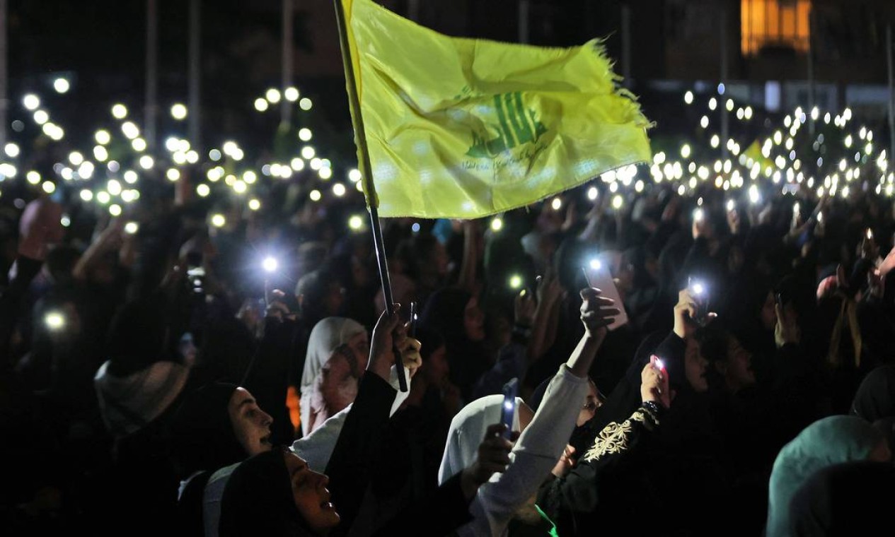 Apoiadores do Hezbollah seguram seus telefones e agitam a bandeira do partido durante uma celebração que marca o 40º aniversário da criação do movimento xiita no subúrbio sul de Beirute Foto: ANWAR AMRO / AFP