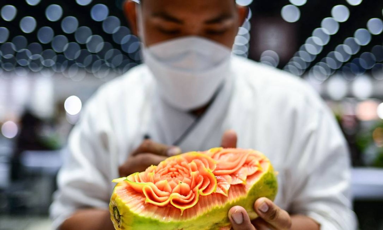 Chef tailandês esculpe flores em um mamão durante competição de escultura de frutas e vegetais em Bangkok. Foto: MANAN VATSYAYANA / AFP