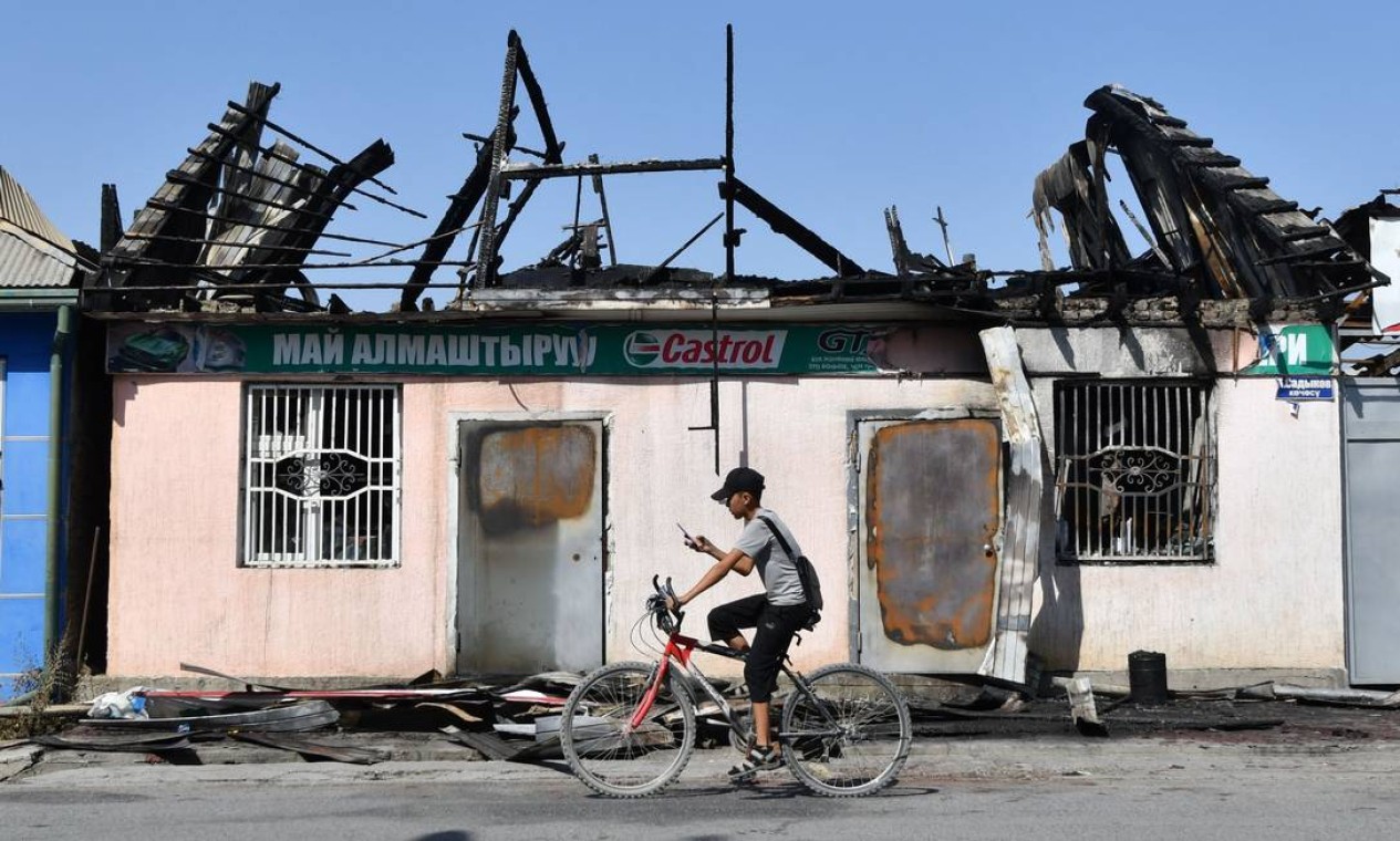 Jovem pedala uma bicicleta em frente a uma loja de óleo de automóveis queimada em Batken, a cerca de mil quilômetros de Bishkek, no Quirguistão. Foto: VYACHESLAV OSELEDKO / AFP