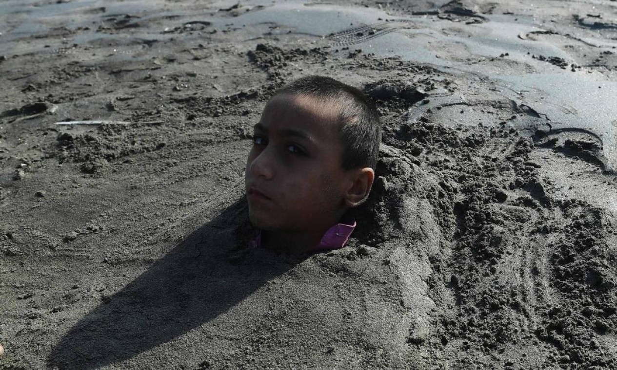 Menino é coberto de areia em uma praia por seus pais sob a crença de que a exposição durante um eclipse solar curará sua doença, em Karachi, Paquistão Foto: ASIF HASSAN / AFP