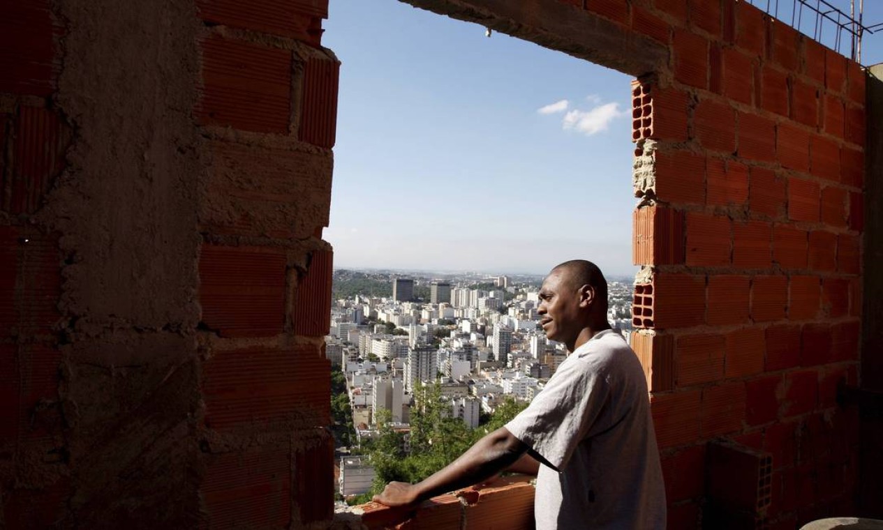 Gustavo dos Santos, na janela da casa em construção, diz que sua casa não foi notificada pela prefeitura Foto: Domingos Peixoto / O Globo