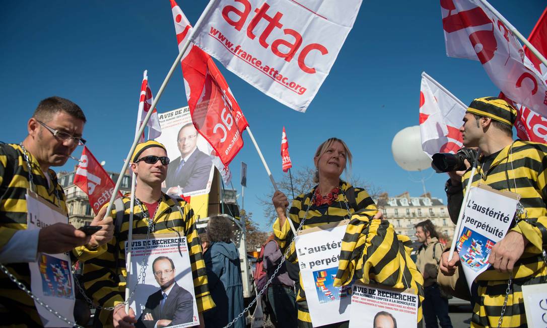 Manifestantes vestidos com trajes de prisioneiros e cartazes com a foto do presidente da França, François Hollande, protestam em Paris Foto: AFP