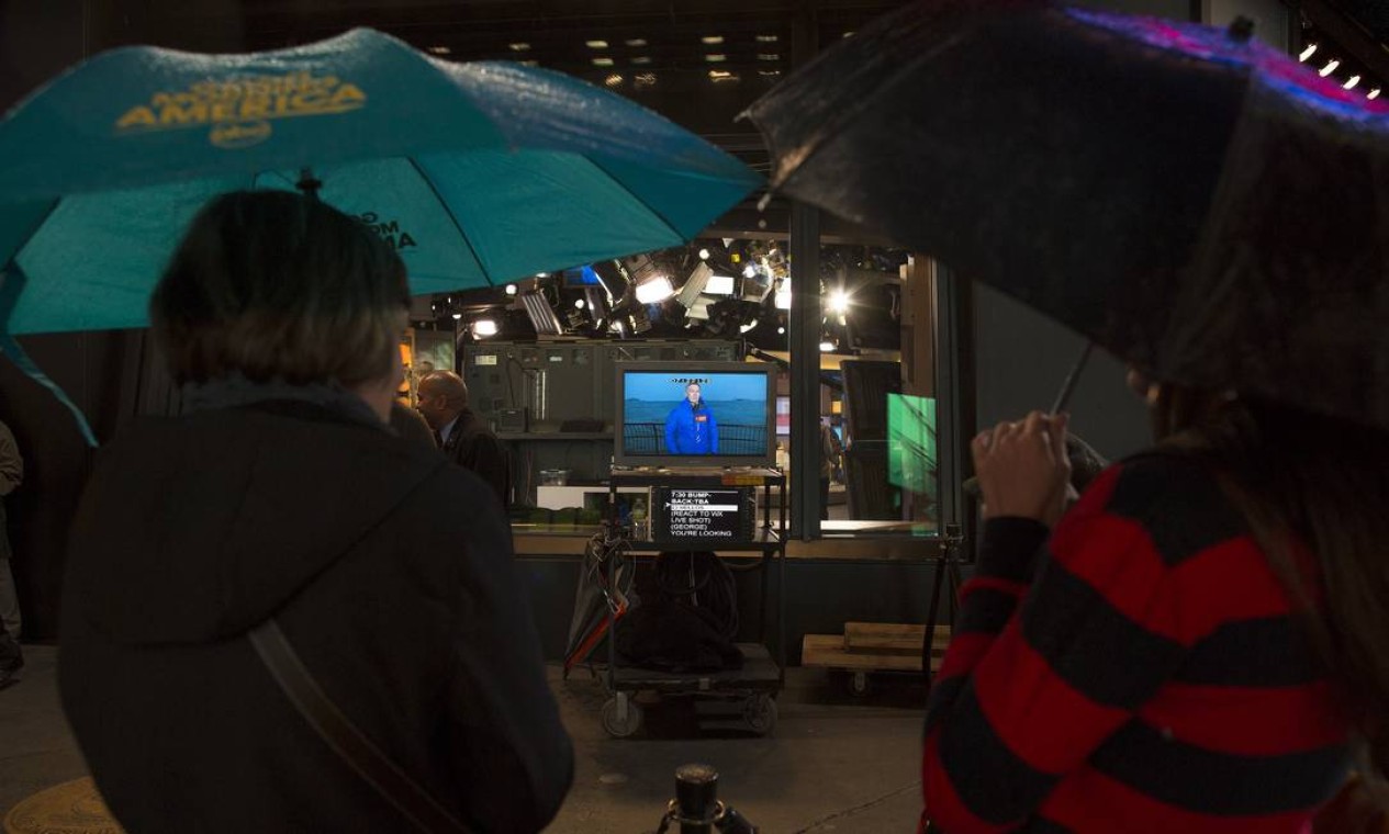Jovens assistem a transmissão do canal de previsão do clima em NY Foto: John Minchillo / AP