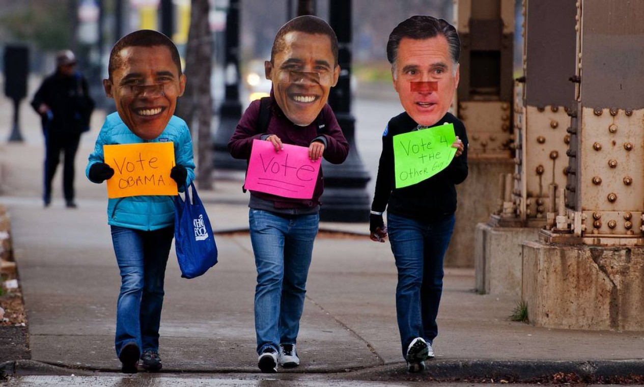 Eleitores de Obama, em Chicago, colocam máscaras com os rostos dos candidatos e seguram cartazes. O do democrata diz: "vote no outro cara" Foto: AFP