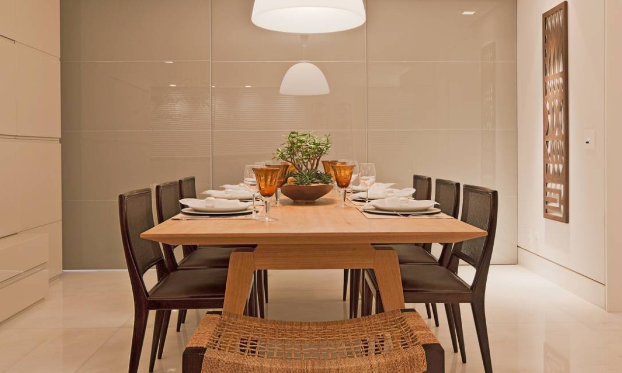 A mesa de jantar em madeira clara contrasta com o piso frio. As cadeiras têm design delicado e encosto em palha, priorizando a leveza Foto: Divulgação