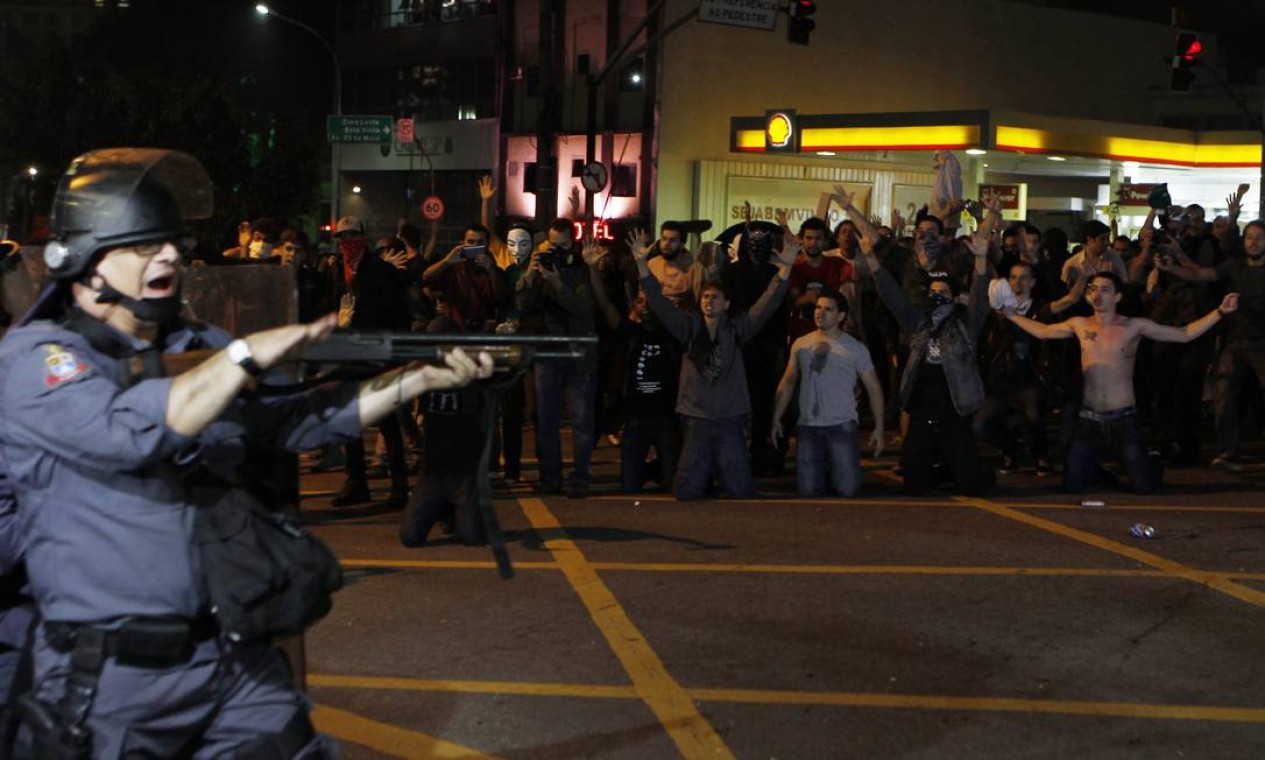Um policial aponta a arma com bala de borracha em direção aos manifestantes, que ficam ajoelhados no meio da rua Foto: Michel Filho / Agência O Globo