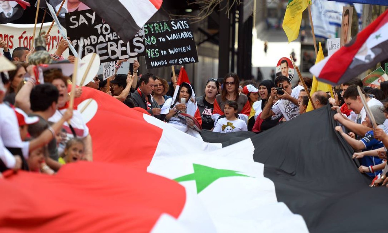 Pessoas cantam durante um protesto em Sydey, na Austrália, contra um possível ataque militar dos EUA contra a Síria, em Sydney . Levando cartazes com os dizeres "Tirem as mãos da Síria" e com o rosto do presidente sírio, Bashar al-Assad Foto: WILLIAM WEST / AFP