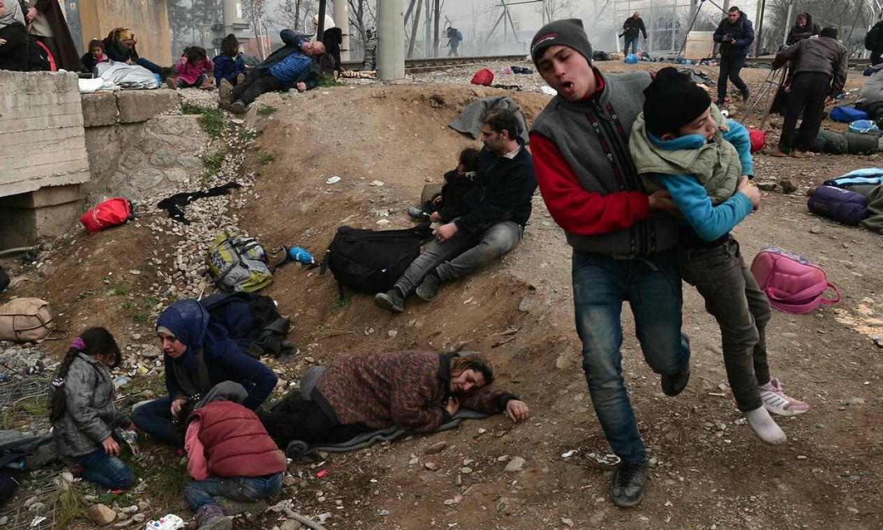Homem foge com criança em meio a confrontos da polícia com refugiados iraquianos e sírios. Autoridades gregas afirmam que mais de 6 mil pessoas têm ocupado a fronteira do país com a Macedônia nos últimos dias. Foto: LOUISA GOULIAMAKI / AFP