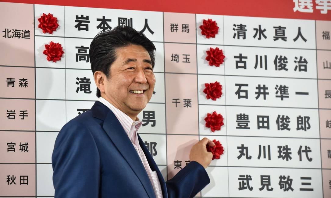 O premier do Japão Shinzo Abe põe flores de papel em um mural indicando os resultados das eleições para a Câmara Alta do Parlamento Foto: KAZUHIRO NOGI / AFP 21-7-19