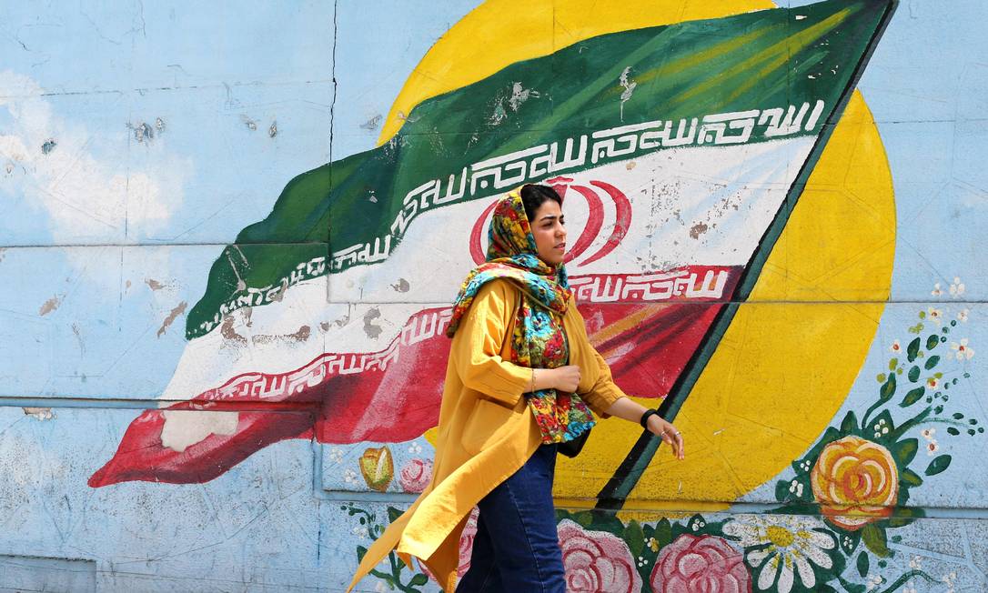 Iraniana passa diante de um mural com a bandeira do país: 40 anos de tensões com os EUA Foto: ATTA KENARE / AFP