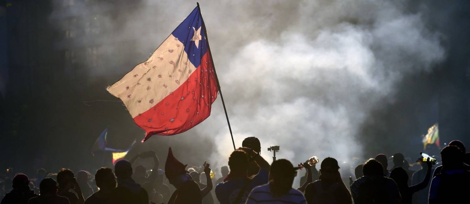 Manifestantes balançam bandeira do Chile em frente a incêndio em Santiago Foto: JOHAN ORDONEZ / AFP 23-11-19