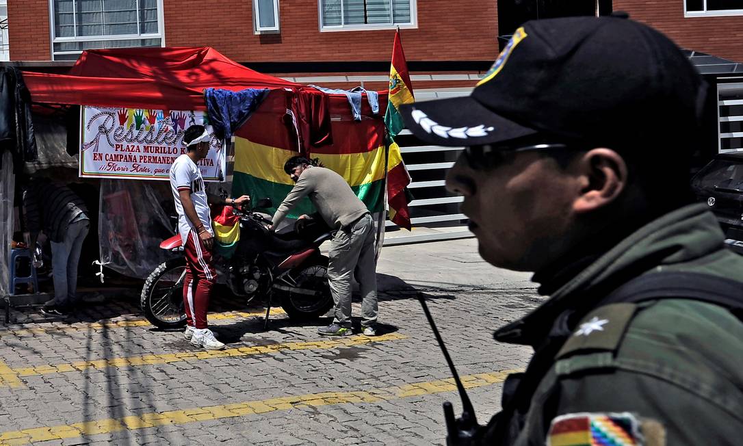 Policial e opositores do ex-presidente boliviano Evo Morales, exilado na Argentina, acampados no condomínio La Rinconada, onde fica a embaixada do México em La Paz Foto: JORGE BERNAL / AFP/30-12-2019