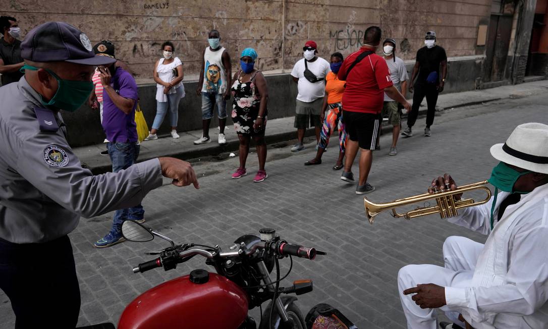 Policial chama a atenção do trompetista Carlos Sanchez a parar de tocar na frente das pessoas que, em fila, esperam para comprar comida: preocupação com a propagação do coronavírus Foto: ALEXANDRE MENEGHINI / REUTERS