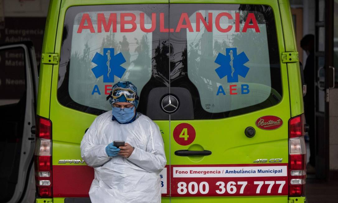 Um profissional da saúde confere seu celular perto de uma ambulância que transportou um paciente com sintomas de Covid-19 em Santiago Foto: MARTIN BERNETTI / AFP
