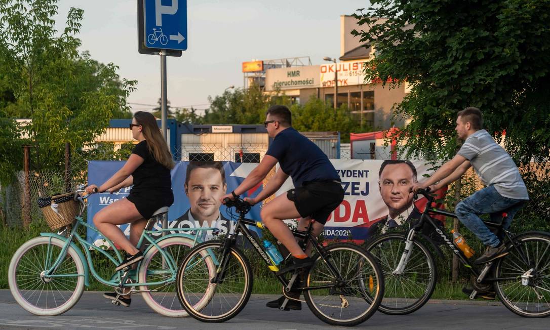 Ciclistas passam em frente a cartazes do opositor Rafal Trzaskowski e do atual presidente Andrzej Duda em um subúrbio de Varsóvia Foto: WOJTEK RADWANSKI / AFP
